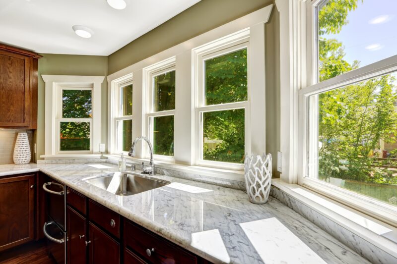 five bay windows above a kitchen sink area with green trees on the outside