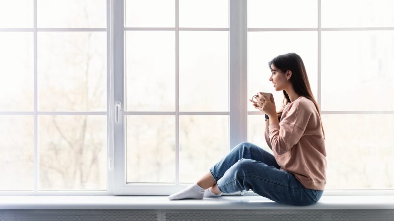 woman sitting in front of a wall of windows while holding a mug