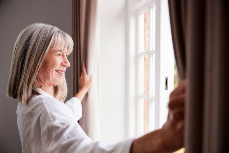 woman holding curtains open and smiling at an open window