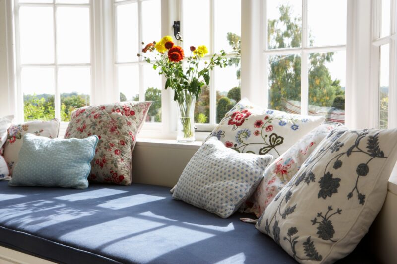 a bay window behind a sitting area with pillows and flowers