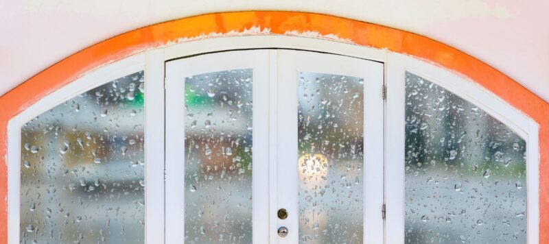 rain on the doors and windows of a home with an orange trim visible above them